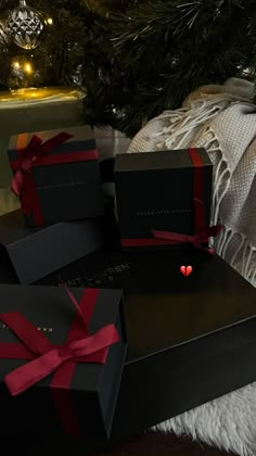 three black boxes with red bows are sitting next to a christmas tree