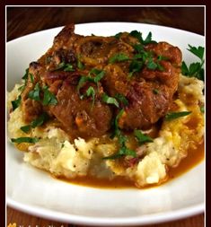 a white plate topped with mashed potatoes and meat covered in gravy, garnished with parsley