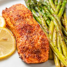 a white plate topped with fish and asparagus next to lemon wedges on a table