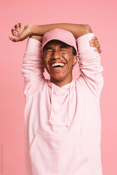 a man wearing a pink hoodie and holding his arms above his head with both hands