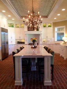 a large kitchen with a center island surrounded by white cabinets and counter tops, along with a chandelier hanging from the ceiling