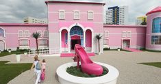 two children are walking in front of a pink building with a slide and palm trees