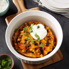 a white bowl filled with mexican food and sour cream on top of a wooden cutting board