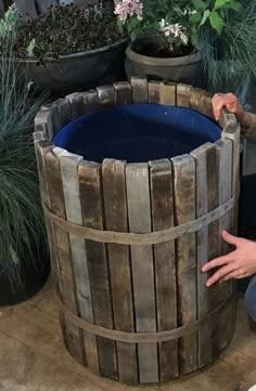 a person kneeling down next to a wooden barrel filled with water and plants in pots