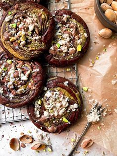 four cookies with nuts and other toppings on a cooling rack next to a spoon