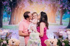 a man and woman holding a baby in front of a cake with teddy bears around them