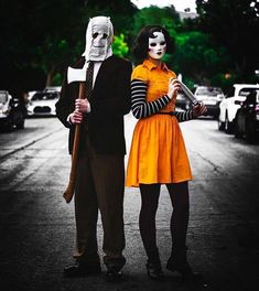 a man and woman dressed in costumes standing next to each other on a street with cars behind them