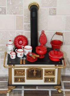 a miniature stove with red pots and pans on it's burner in front of a brick wall