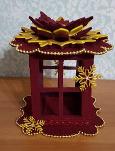 a red and gold decoration on a wooden table with snowflakes in the background