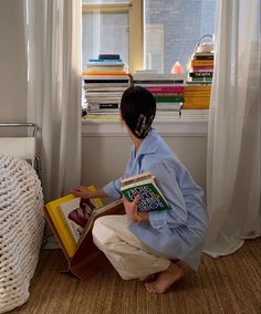 a woman kneeling down reading a book in front of a window with bookshelves