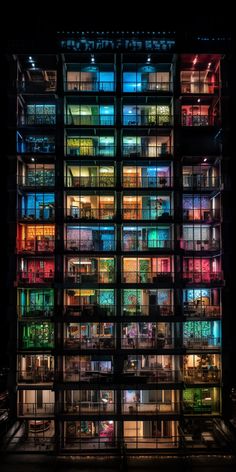 the building is lit up at night with brightly colored lights on it's windows