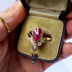 a person holding a ring in their hand with a red stone on the middle and white stones at the bottom