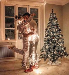 a man and woman standing in front of a christmas tree with their arms around each other