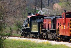 a red and black train traveling down tracks next to a lush green hillside covered in trees