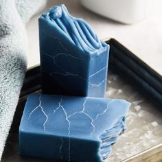 three blue soap bars stacked on top of each other in front of a cup and tray