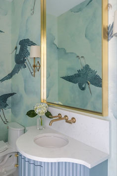 a bathroom with blue and white wallpaper, gold framed mirror, sink and toilet