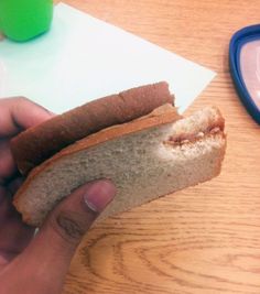 a person holding a sandwich in their left hand on top of a wooden table next to a blue plate