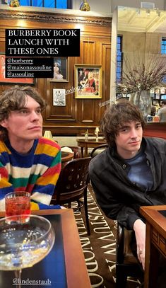 two young men sitting at a table in a restaurant, one is looking off to the side