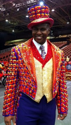 a man in a colorful suit and top hat at a convention or show, smiling for the camera