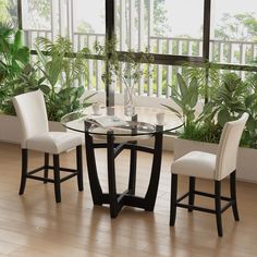 a glass table with white chairs in front of a plant filled wall and window sill