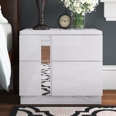 a white dresser with flowers and a clock on it's side table next to a bed