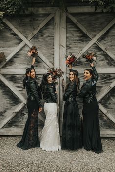 three women in black dresses standing next to each other with their arms up and one holding flowers