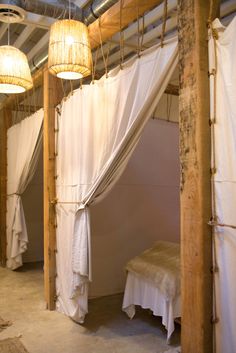 a room with white curtains and lights hanging from it's ceiling next to a bed