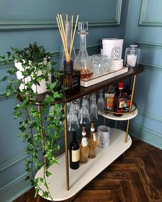 a bar cart filled with liquor bottles and glasses on top of a wooden floor next to a potted plant