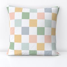 a white pillow with multicolored squares on the front and back, sitting on a table