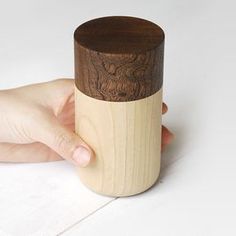 a person holding a wooden cup in their left hand on a white surface with wood grain