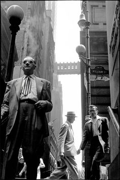 three men in suits and ties walking down the street next to tall buildings with signs on them