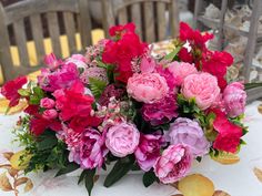 pink and red flowers sitting on top of a table next to an empty chair in front of a white tablecloth