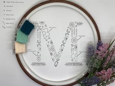 a cross stitch pattern with the letter m on it next to some purple and green flowers