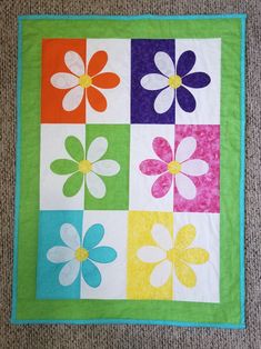 a multicolored flower quilt is displayed on the floor in front of a carpet