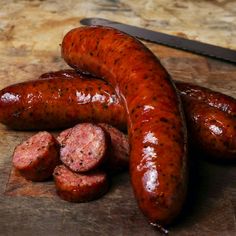 two sausages on a cutting board next to a knife