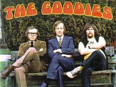 the goodies sitting on a park bench in front of a bush with their arms crossed