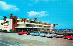 an old photo of cars parked in front of a motel on the beach with palm trees