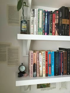 there are many books on the shelves with a clock next to it and two vases