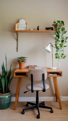 a desk with a chair, potted plant and books on it in front of a white wall