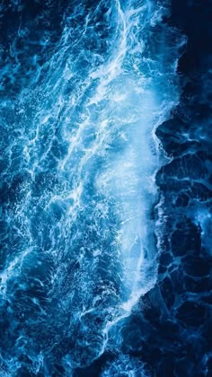 an aerial view of the ocean with waves crashing on it's shore and dark blue hues