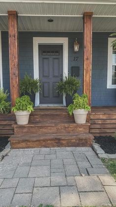 two potted plants sit on the front steps of a blue house with white trim