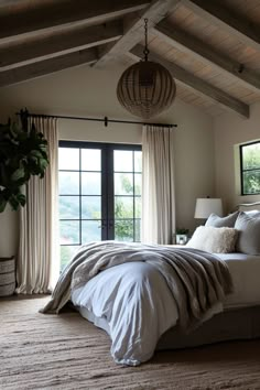 a large bed sitting under a window next to a wooden ceiling mounted light above it