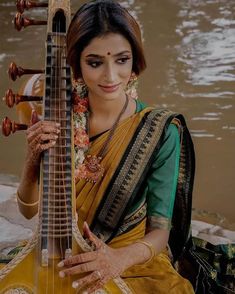 a woman sitting on the ground holding a musical instrument in her hands and looking at the camera