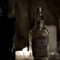 a bottle of bourbon whiskey sitting on top of a table next to candles and tea lights