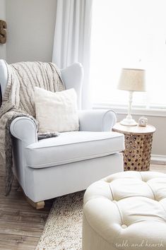 a living room with a chair, ottoman and lamp on the side table in front of a window