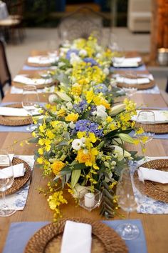 a long table with yellow and blue flowers on it is set for an outdoor dinner