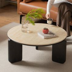 a woman sitting on a couch reading a book and holding a coffee table with a plant in it