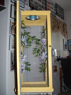 a yellow clock with purple flowers and green leaves on the front is hanging from a wall