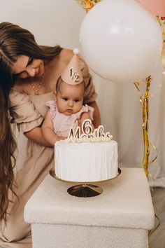 a woman holding a baby in front of a cake