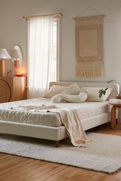 a white bed sitting in a bedroom on top of a hard wood floor next to a window